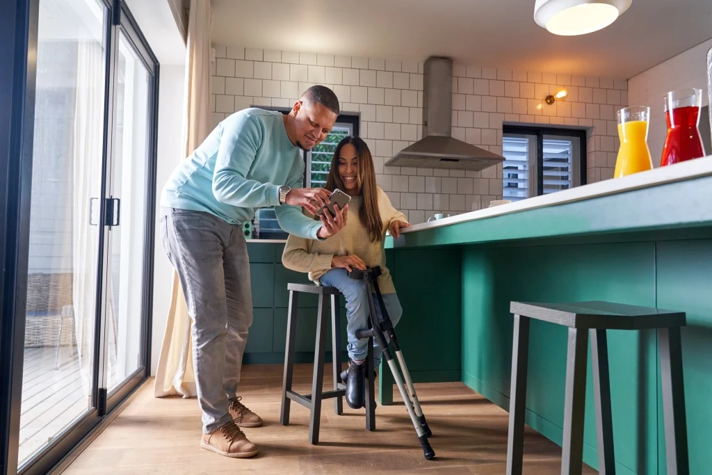 Support worker and disabled woman looking at mobile phone in kitchen